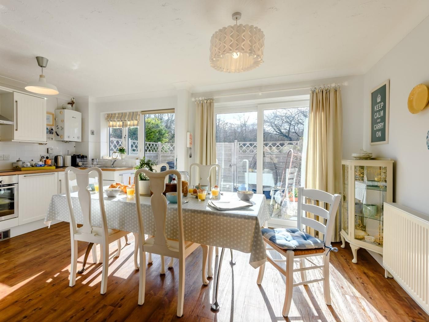 Una cocina luminosa con armarios blancos, una mesa de comedor con sillas y vistas al exterior a través de amplios ventanales.