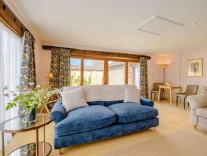 Ein gemütliches Wohnzimmer mit einem blauen Sofa, einem Glastisch und einem Essbereich mit Tisch und Stühlen.