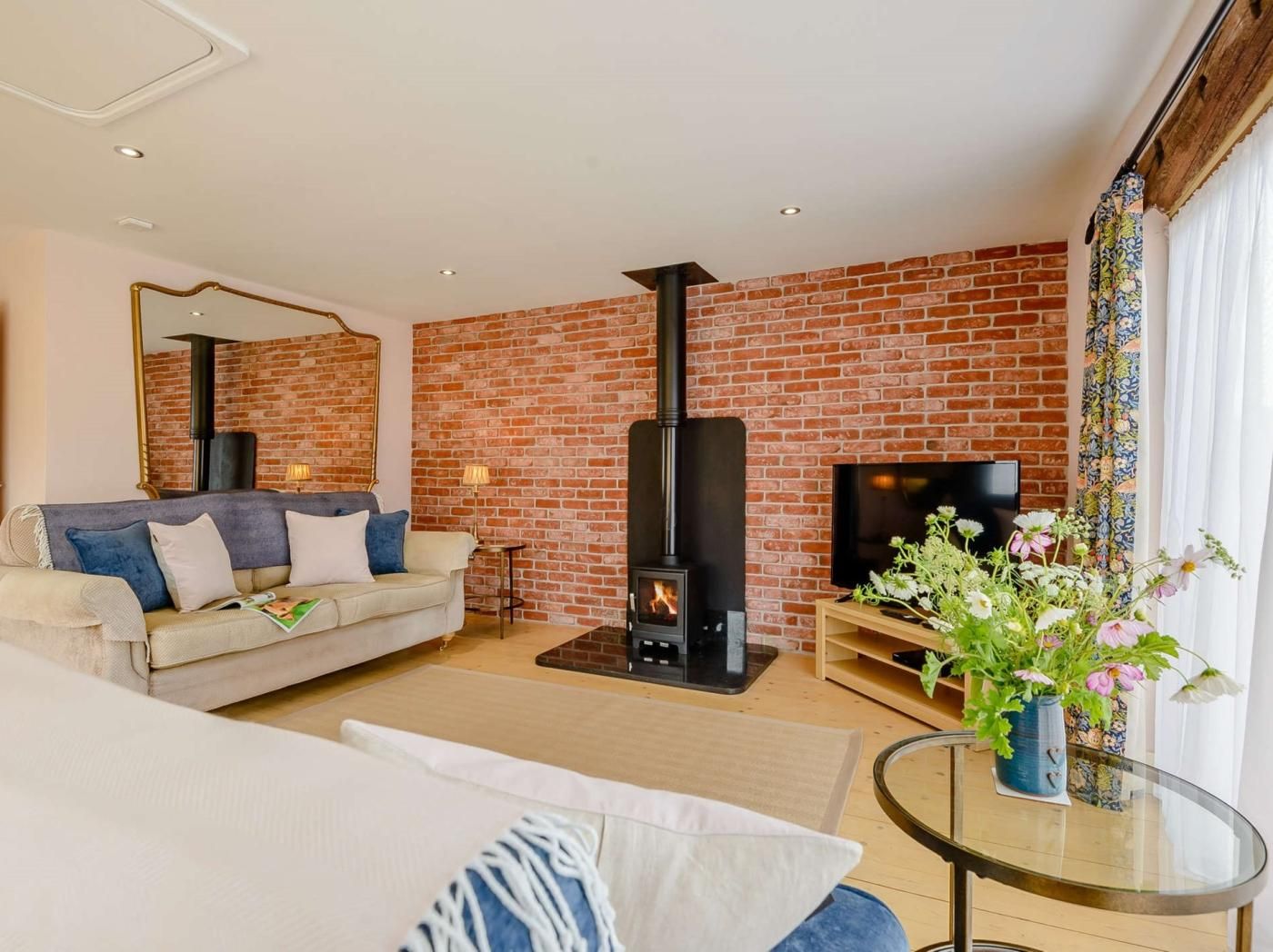 A living room with a brick wall, a sofa, a TV, a fireplace, and a glass table with flowers.
