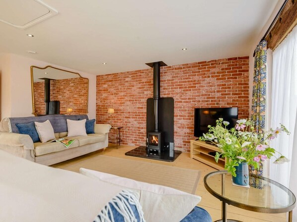 Ein Wohnzimmer mit Backsteinwand, einer Couch, einem Fernseher, einem Kamin und einem Glastisch mit Blumen.