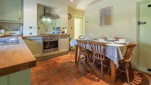 A kitchen with a stove, oven, and a dining table set for four. - 3 Bed in King's Lynn (oc-kt097) (Ingoldisthorpe)