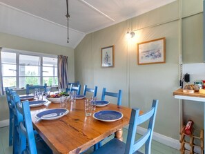 Uma sala de jantar com uma mesa de madeira posta para seis pessoas, cadeiras azuis e quadros nas paredes.