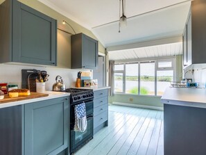 Eine moderne Küche mit grauen Schränken, einem Herd und einem großen Fenster mit Blick ins Freie.