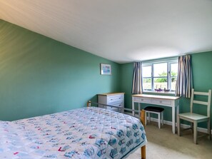 Ein Schlafzimmer mit einem Bett, einem Schreibtisch, einem Stuhl und einem Fenster mit Vorhängen.