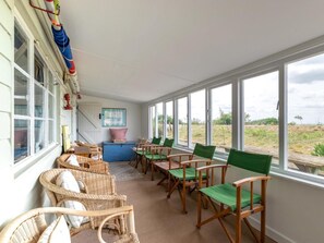 Ein sonnendurchflutetes Zimmer mit Korbmöbeln, einem blauen Sofa und Blick auf die Landschaft.