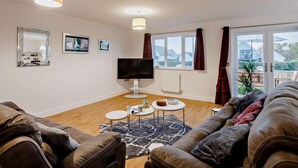 A living room with a sofa, a TV, a fireplace, and a view of the outside. - 3 Bed in Bideford (oc-90319) (Westward Ho!)