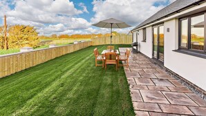 A patio with a table and chairs, a barbecue grill, and a wooden fence. - 3 Bed in Bideford (oc-90319) (Westward Ho!)