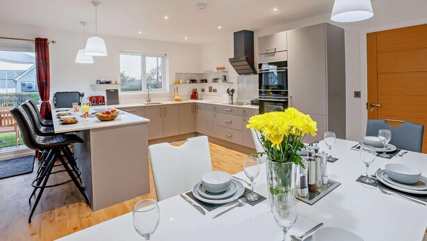 A modern kitchen with a dining area, featuring a central island, pendant lighting, and a view of the outdoors. - 3 Bed in Bideford (oc-90319) (Westward Ho!)