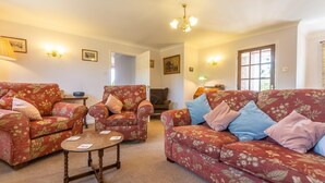 A living room with floral-patterned sofas, a wooden coffee table, and a chandelier. - 2 Bed in Weasenham (oc-kt103) (Weasenham)