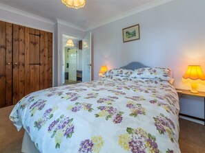 A bedroom with a floral bedspread, two bedside lamps, a framed picture on the wall, and a wooden wardrobe. - 2 Bed in Weasenham (oc-kt103) (Weasenham)
