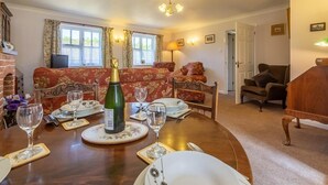 A dining area with a wooden table set for a meal, a sofa in the background, and a fireplace. - 2 Bed in Weasenham (oc-kt103) (Weasenham)