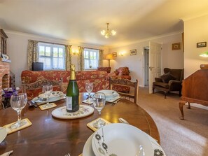 A dining area with a wooden table set for a meal, a sofa in the background, and a fireplace. - 2 Bed in Weasenham (oc-kt103) (Weasenham)