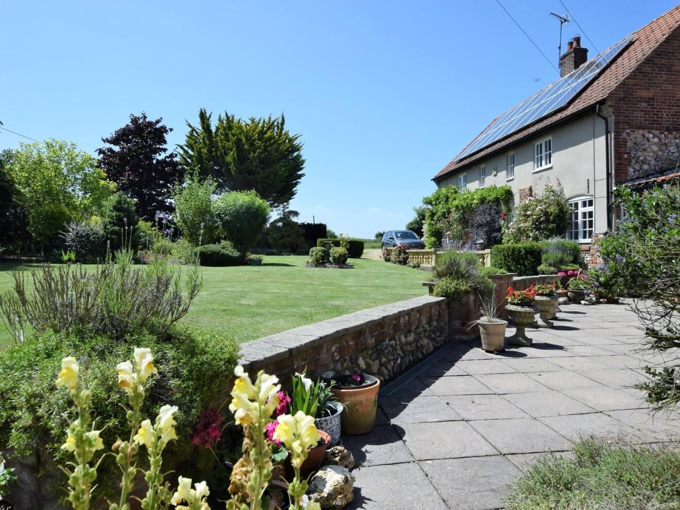 A residential garden with a stone wall, potted plants, and a house with a sloped roof.