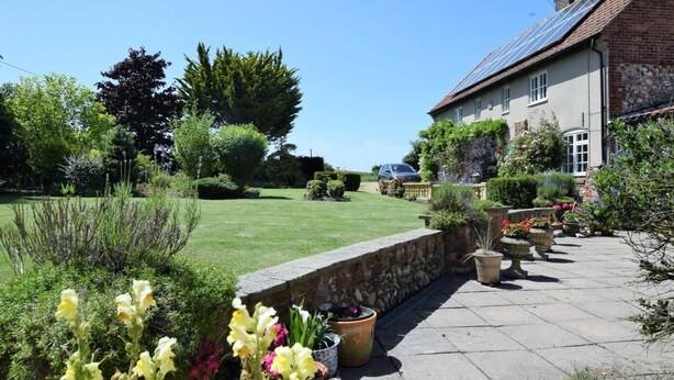 A residential garden with a stone wall, potted plants, and a house with a sloped roof. - 2 Bed in Weasenham (oc-kt103) (Weasenham)