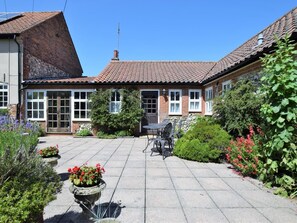 A courtyard with a patio table and chairs, surrounded by a brick house with a tiled roof. - 2 Bed in Weasenham (oc-kt103) (Weasenham)
