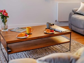 A wooden coffee table with a magazine, a yellow mug, a croissant, and strawberries. - 3 Bed in Bideford (oc-90335) (Westward Ho!)
