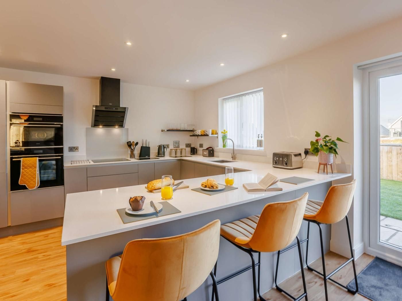 A modern kitchen with a central island, bar stools, and a view of the outdoors.