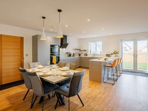 A modern kitchen with a dining area, a bar, and a sliding glass door to a backyard. - 3 Bed in Bideford (oc-90335) (Westward Ho!)