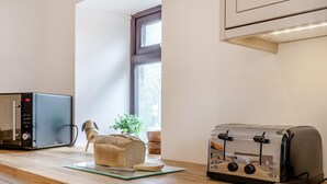 Een keuken met een magnetron, broodrooster, een brood en een raam.