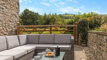 An outdoor seating area with a stone wall, a wooden gate, and a view of a green landscape.