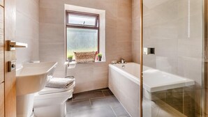 Een moderne badkamer met bad, toilet en wastafel, voorzien van een groot raam en een douchegedeelte.