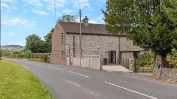 A stone house with a gated driveway, surrounded by greenery and a clear sky.