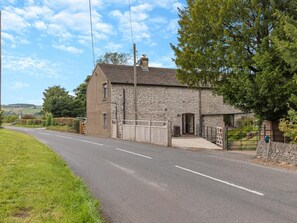 A stone house with a gated driveway, surrounded by greenery and a clear sky.