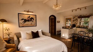 Ein Schlafzimmer mit einem großen Bett, einer Sitzecke mit einer Bank, einem Essbereich mit Stühlen, einer Küche mit Herd und einer Kristallleuchtre.