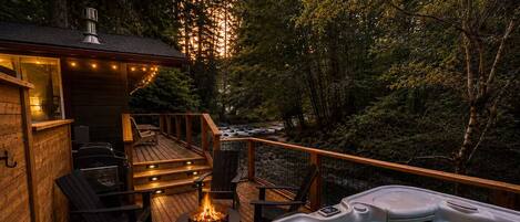 A wooden deck with a hot tub, outdoor seating, and a fire pit.