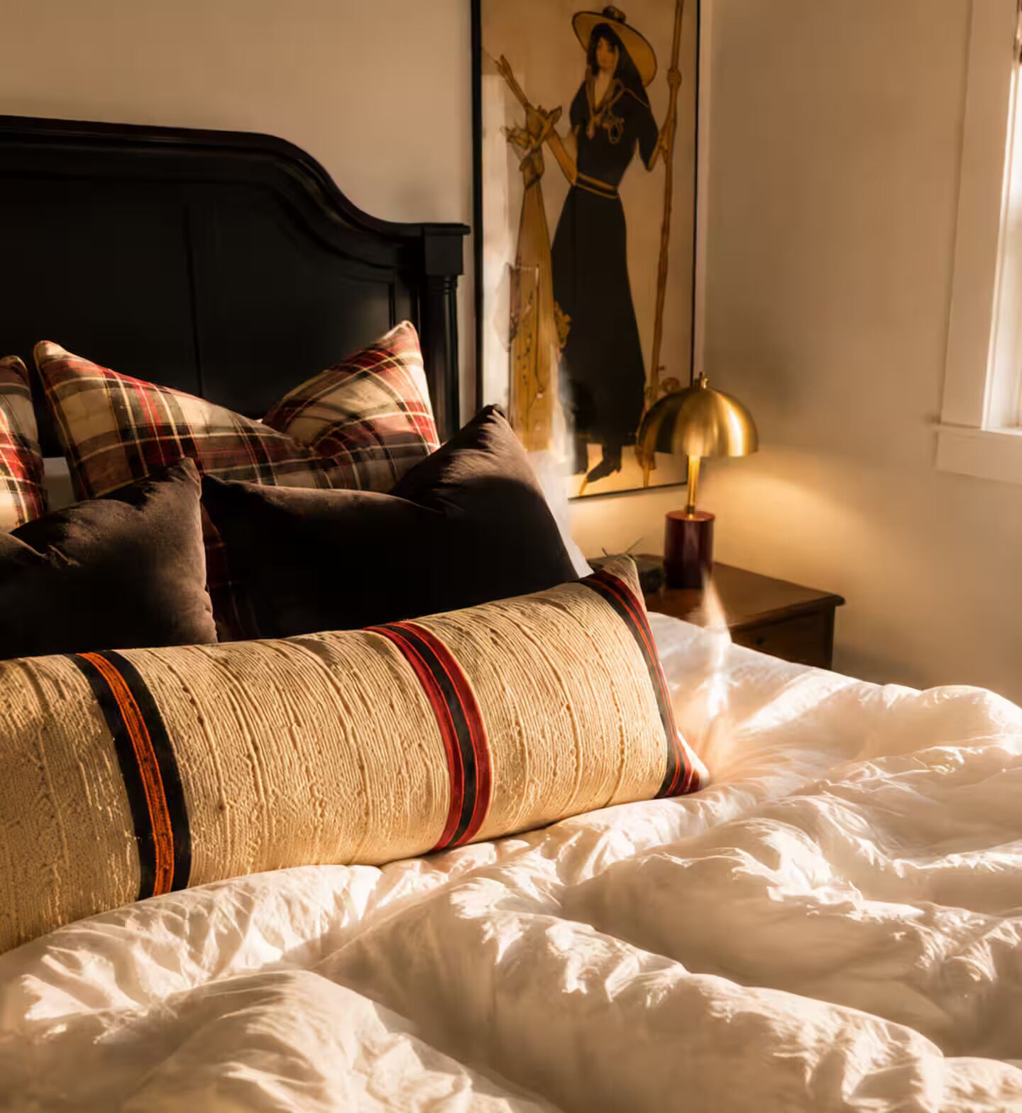A bed with multiple pillows, a headboard, a wall-mounted lamp, and a framed picture.