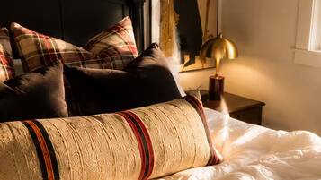 A bed with multiple pillows, a headboard, a wall-mounted lamp, and a framed picture.
