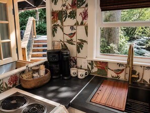 A kitchen with a coffee maker, mugs, and a wooden bowl on the counter. - Magical Retreat Over Morse Creek with Hot Tub (Port Angeles)