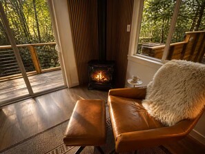 A cozy room with a leather chair, a small table with a cup, and a wood-burning stove. - Magical Retreat Over Morse Creek with Hot Tub (Port Angeles)