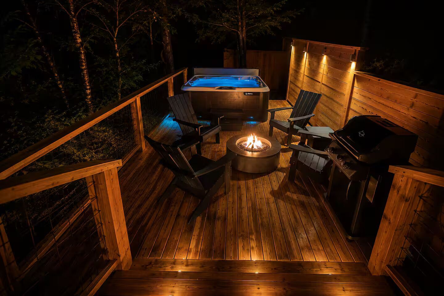 A wooden deck with a hot tub, a fire pit, and a grill.