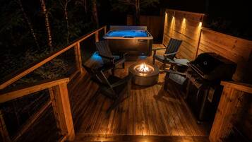 A wooden deck with a hot tub, a fire pit, and a grill.