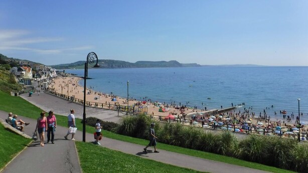 Eine Küstenpromenade mit Strand, einem Glockenturm und freiem Blick auf das Meer.