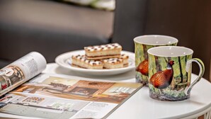 Ein Tisch mit einer Kuchenspeise, zwei Tassen und einer Zeitschrift.