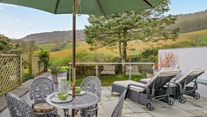 Eine Terrasse im Freien mit Tisch und Stühlen, einem großen Sonnenschirm und Blick ins Grüne.