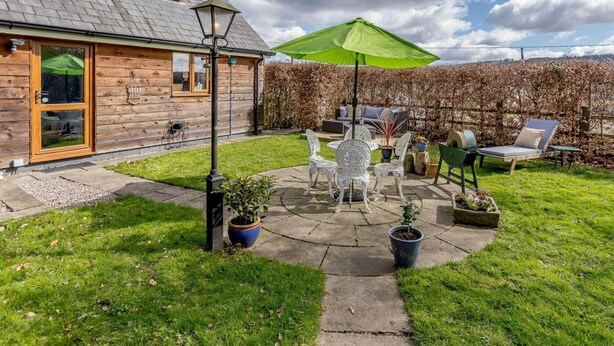 A wooden house with a patio, outdoor furniture, and a green umbrella. - 1 Bed in Lydney (oc-43724) (Lydney)