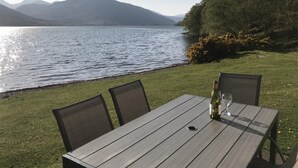 Ein Tisch mit Stühlen am See, eine Weinflasche und ein Glas.