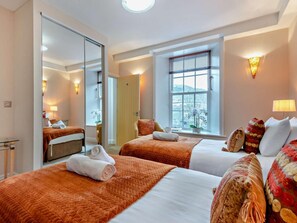 Ein Hotelzimmer mit zwei Betten, einem großen Spiegel, einem Fenster mit Jalousien und einer Wandlampe.