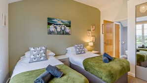 Hotellihuone, jossa on kaksi sänkyä, lammasaiheinen taulu, peili ja näkymä ulos.