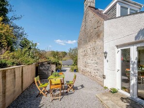 Une terrasse avec une table et des chaises, un mur en pierre et un bâtiment doté d’une fenêtre et d’une porte.