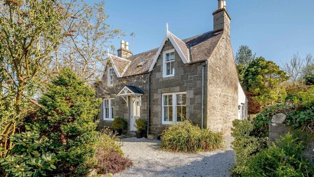 A stone house with a gravel driveway, surrounded by greenery. - 2 Bed in Kippford (oc-81129) (Colvend)