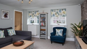 A living room with a sofa, a blue armchair, a bookshelf, and a radiator. - 2 Bed in Brecon (oc-bn436) (Brecon)