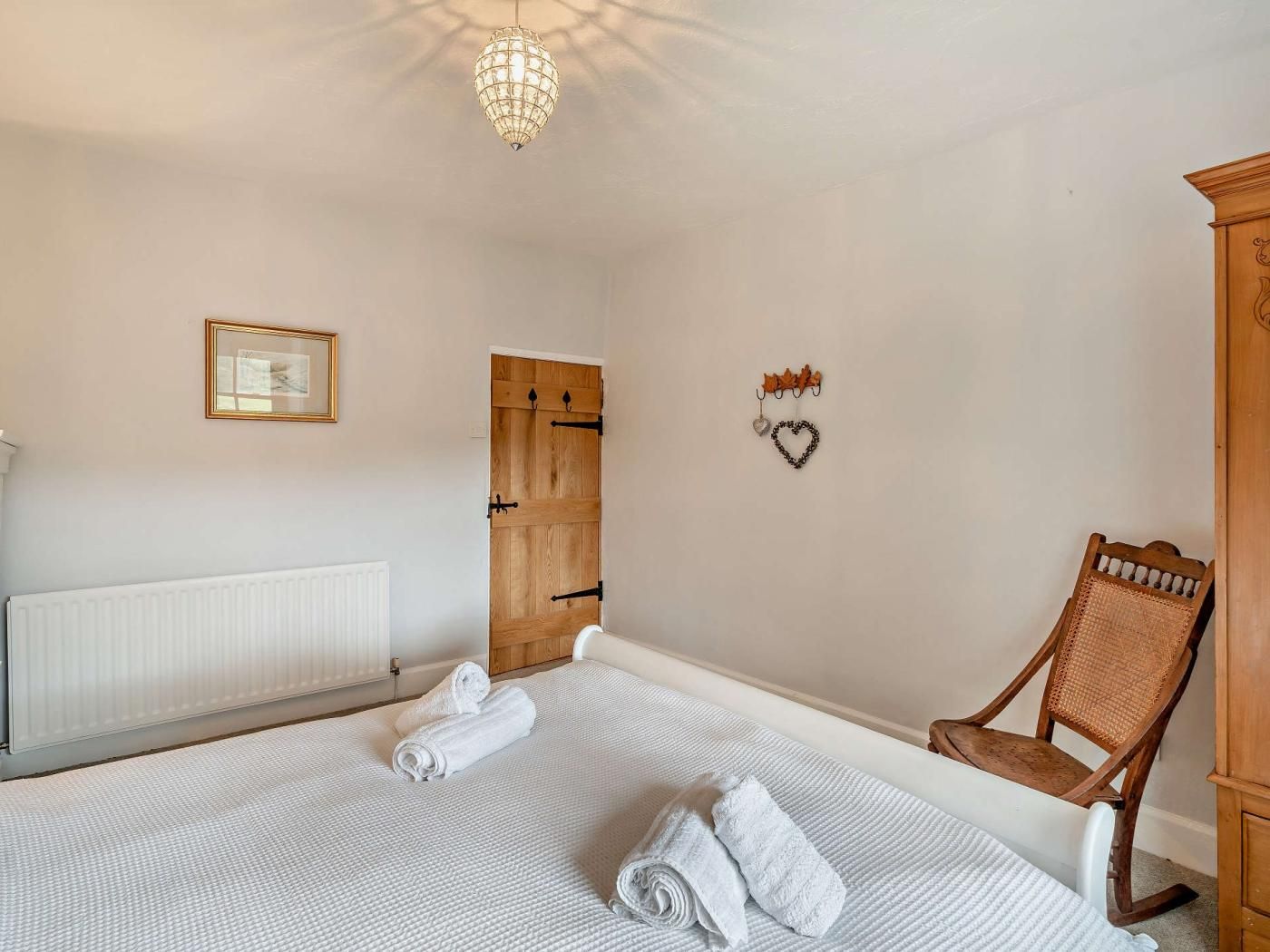 Un dormitorio con cama, puerta de madera, una silla, radiador y candelabro.
