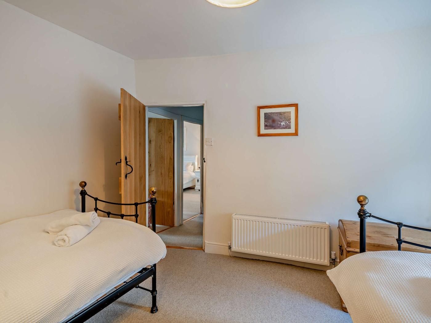 A bedroom with two beds, a radiator, and a door leading to another room.