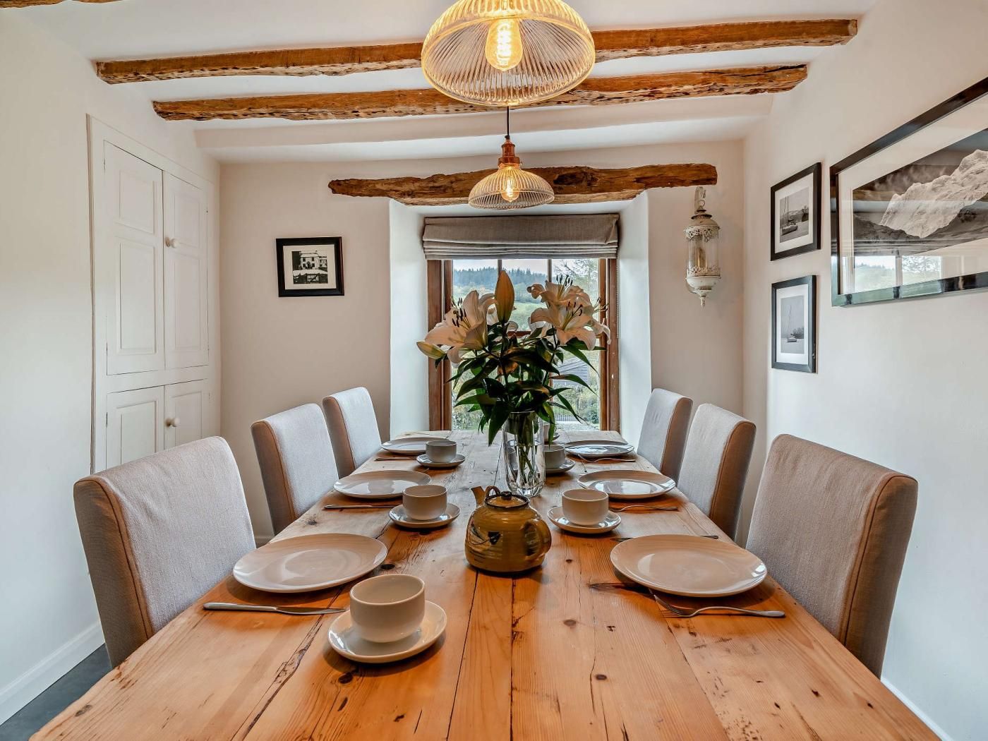Une salle à manger avec une table en bois mise pour six personnes, entourée de chaises, et un vase de fleurs placé au centre.