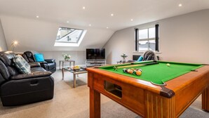 Ein gemütliches Wohnzimmer mit Billardtisch, einer Couch und einem Fernseher.