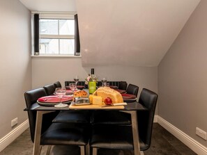 A dining area with a table set for four, including plates, glasses, a bottle of wine, and a loaf of bread. - 3 Bed in Keswick (oc-83170) (Keswick)